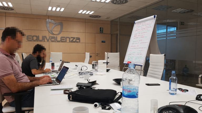 Sala de reuniones de las oficinas de Equivalenza, con dos personas trabajando con portátiles y un rotafolio lleno de anotaciones.