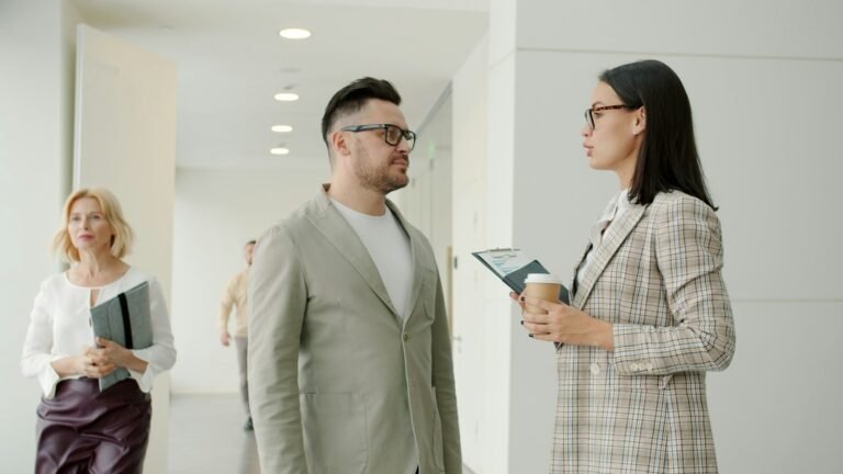Dos compañeros conversan de manera informal en un pasillo de oficina; una de las personas sostiene un café. Fotografía de Vitaly Gariev en Unsplash.